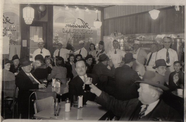 A packed American Coney Island dining room in the 1940s, men in fedoras at the tables and staff in white paper hats behind the counter